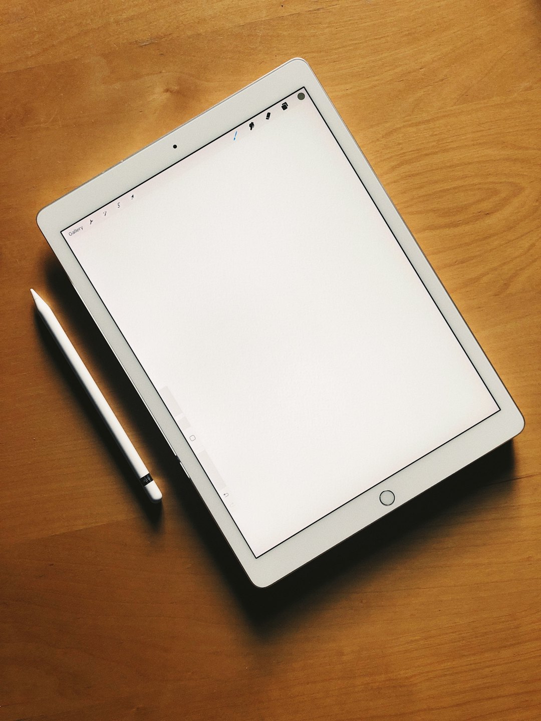 Na drevenom stole leží biely digitálny tablet so stylusom.
